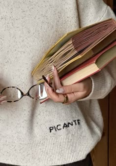 a woman holding a stack of books with glasses on her hands and reading material in the other hand