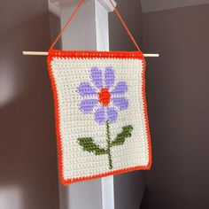 a crocheted flower hanging from a hook on a door handle with an orange and white frame