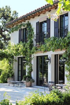 a white house with lots of windows and plants on the outside wall, surrounded by greenery