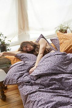 a woman laying in bed with purple sheets