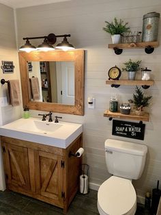 a white toilet sitting under a bathroom mirror next to a wooden sink vanity with open shelves