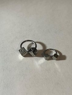 two silver rings sitting on top of a white table next to each other, one with a heart and the other with an arrow