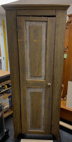 an old wooden armoire sitting on top of a floor next to a trash can