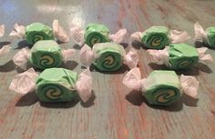 green and white candy wrapped in tissue paper on a wooden table with other candies