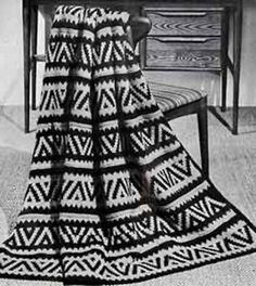 a black and white photo of a crocheted blanket on a chair with a table in the background