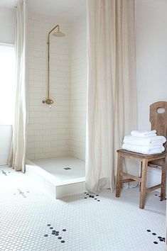 a white bathroom with black and white tile flooring, shower curtain, and wooden chair