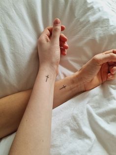 a woman's arm with a cross tattoo on it and her hand resting on the pillow