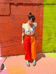 a woman standing in front of a colorful wall with her hands on her hips and looking down at the ground