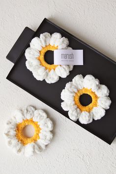 two crocheted flowers sitting on top of a black tray next to each other