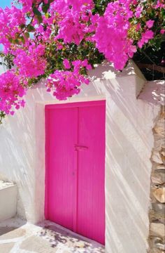 a bright pink door is in front of a white building with flowers on the outside