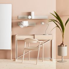 a desk with a chair and a potted plant on it in front of a pink wall