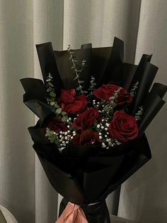 a bouquet of red roses and baby's breath wrapped in black paper on a table