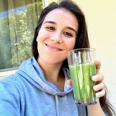 a woman is holding a glass with green liquid in it and smiling at the camera