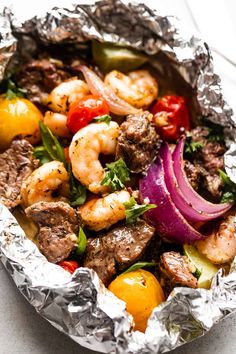 a close up of food in tin foil with shrimp and veggies on it