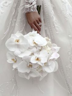 a woman in a wedding dress holding a bouquet of white orchids with her hand