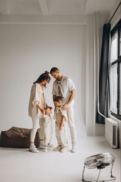 a family standing in front of a window with their arms around each other and looking at something on the floor