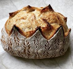 a loaf of bread sitting on top of a white paper covered tablecloth with an intricate design