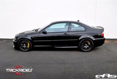 a black car parked in front of a white wall with yellow rims on it