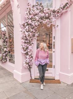 a woman standing in front of a pink building with flowers on the door and windows