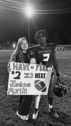 two people holding a sign that says have no fear 25 is here and football helmets are in the background