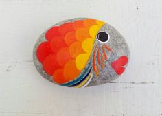 a rock painted like a fish with multicolored feathers on it's face