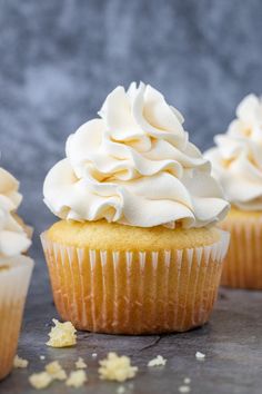 three cupcakes with white frosting and sprinkles on a table