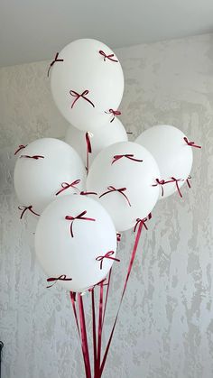 white balloons with red string tied to them in a vase on a table next to a wall