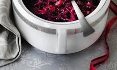 a white bowl filled with red cabbage on top of a table next to a spoon