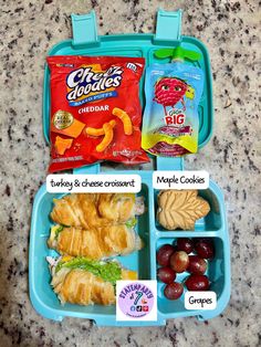 a lunch box with grapes, turkey and cheese croissants in the middle