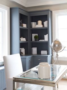 a glass table with white chairs and shelves in the background