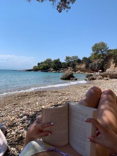 a woman reading a book on the beach with her feet propped up in front of an open book