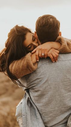 a man and woman embracing each other in the middle of an open field with brown grass