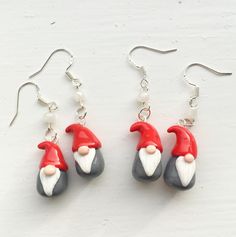 three gnomes wearing red and white hats are hanging from silver earwires on a white surface