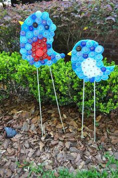 two blue birds made out of plastic bottle caps sitting on top of leaves in front of bushes