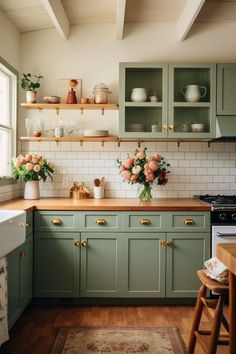 a kitchen with green cabinets and white tile backsplash, wood flooring and flowers in vases on the counter