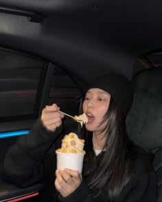 a woman eating food out of a paper cup in the back seat of a car