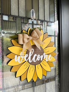 a welcome sign hanging on the side of a building with a sunflower in front