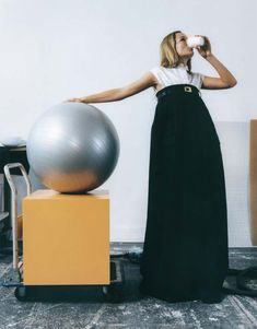 a woman drinking from a bottle next to an exercise ball