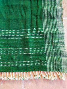 a green and white blanket laying on top of a pink tile floor next to a brick wall