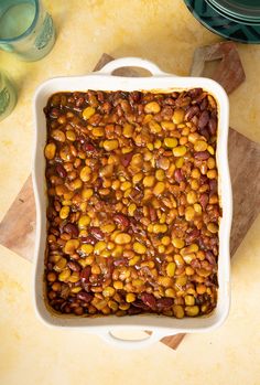 a casserole dish filled with beans on top of a wooden cutting board