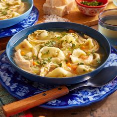 two bowls filled with pasta and vegetables on top of a blue plate next to bread