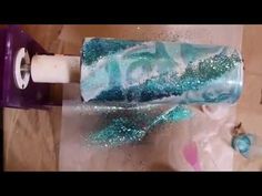 a toilet paper roll with blue and green glitter on it sitting on top of a wooden floor