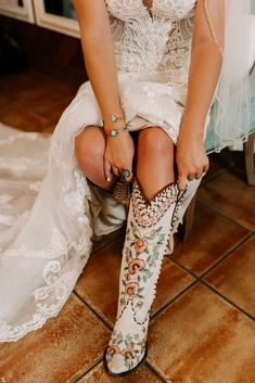 a woman sitting on top of a tiled floor next to a white dress and cowboy boots