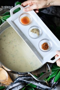 someone is holding a tray with three small bowls and sauces in it on top of a wooden table