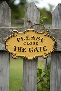 a yellow sign that says please close the gate on a wooden fence with green grass in the background