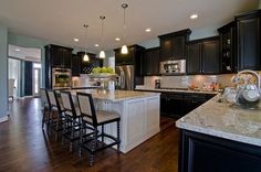 a large kitchen with black cabinets and white counter tops, along with an island in the middle