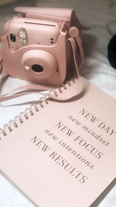 a pink camera sitting on top of a notebook next to a pen and paper that says new today