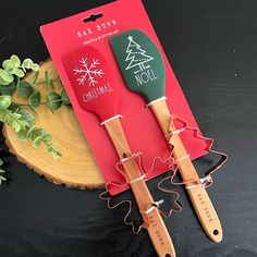 two spatulas with christmas designs on them sitting next to a card and plant