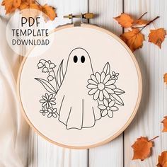 a cross stitch pattern with an image of a ghost and flowers in the hoop on a white wooden background