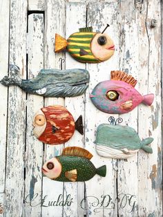 four colorful fish are hanging on the side of a white wooden planked wall,